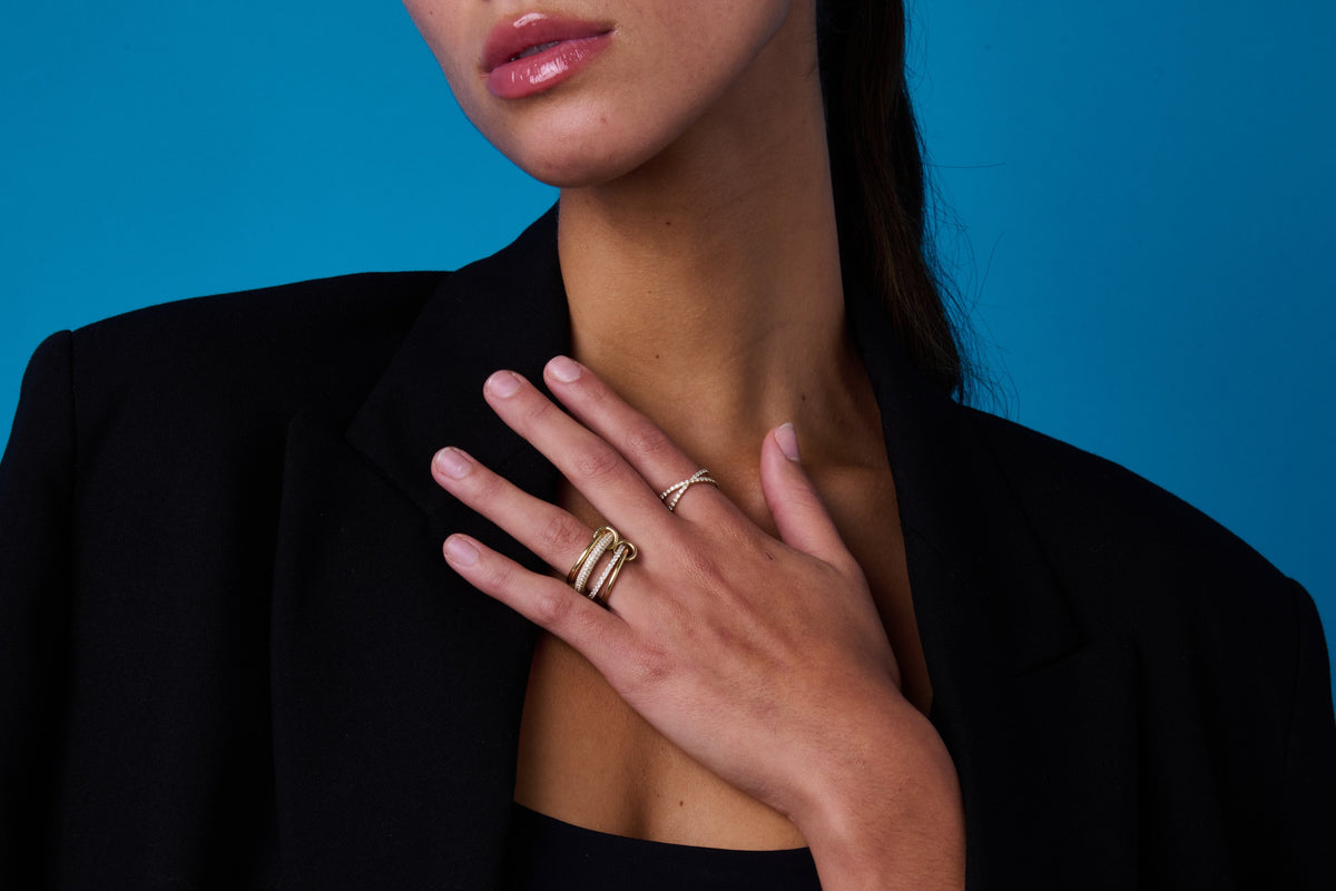 Hand wearing pavé diamond rings against E’LHAA blue