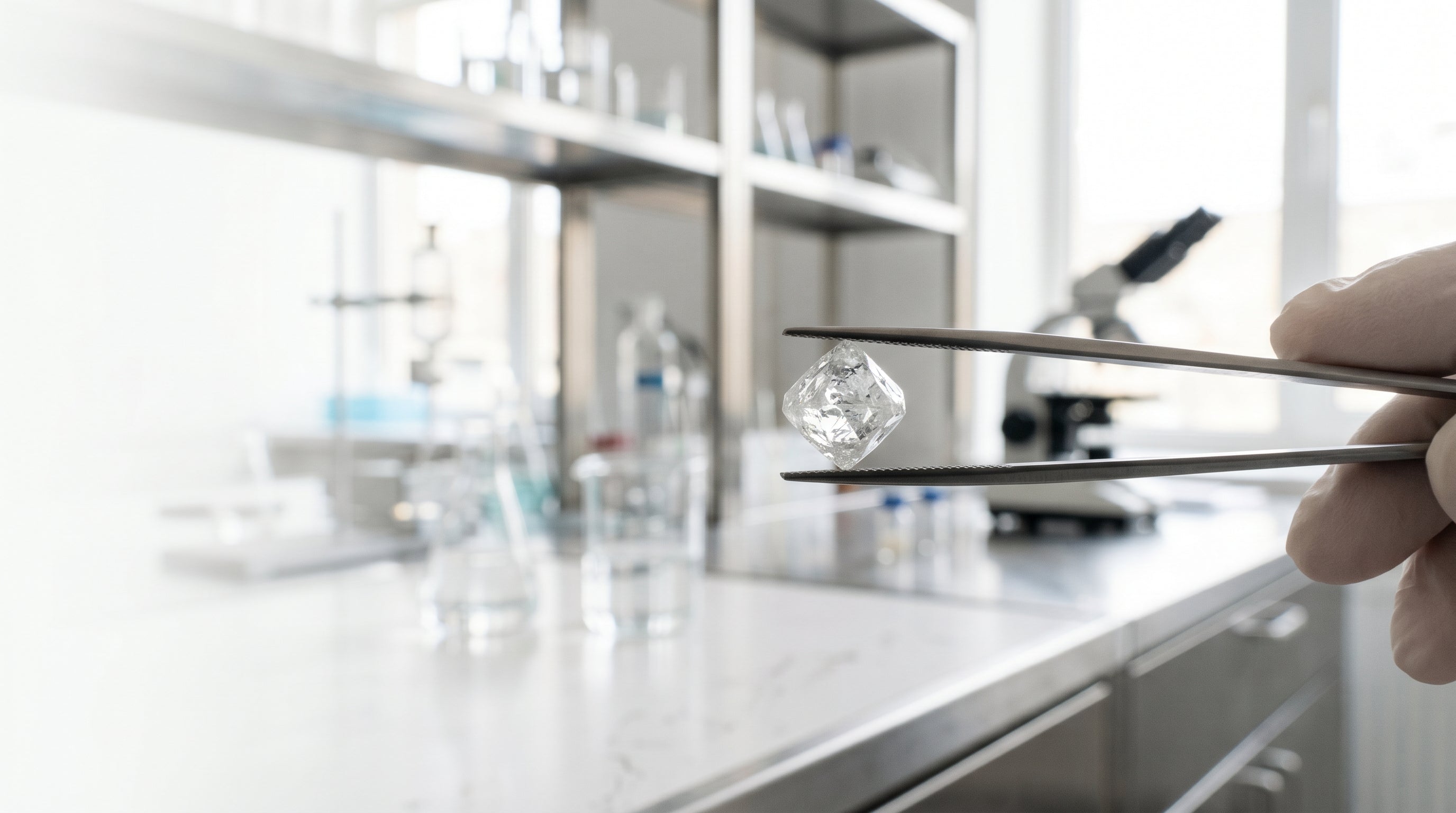 Rough lab-grown diamond crystal held in tweezers in a bright laboratory